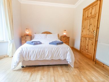 A bedroom with a bed with white sheets and two folded towels on it two wooden bedside tables with lamps a wooden door and a window with curtains at Cloughoge House in Kilrush County Clare