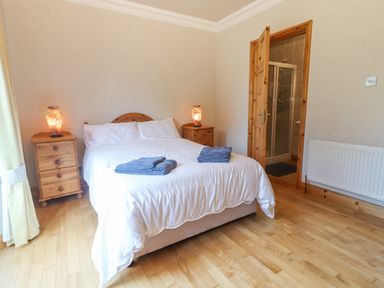 A bedroom with a double bed with white bedding two bedside tables with lamps wooden floor and an en suite bathroom at Cloughoge House Kilrush County Clare