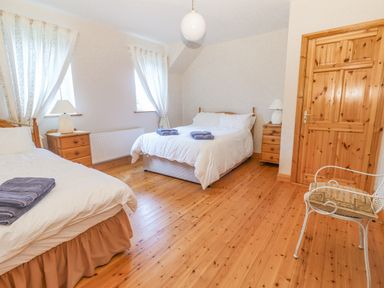 A bedroom with two beds wooden flooring wooden bedside tables with lamps and a wooden door at Cloughoge House in Kilrush County Clare
