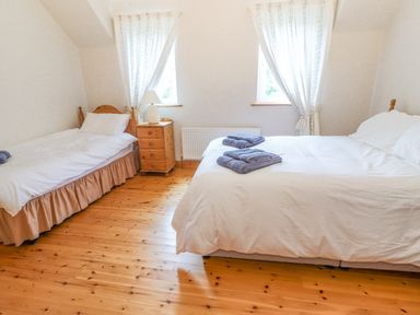A bedroom with two beds a wooden nightstand and two windows at Cloughoge House in Kilrush County Clare
