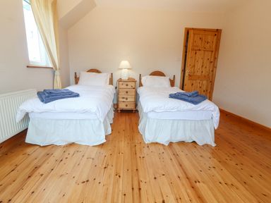 A bedroom with two single beds a wooden nightstand with lamp and a wooden door at Cloughoge House in Kilrush County Clare
