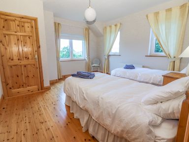 A bedroom with two single beds wooden floor and three windows with curtains at Cloughoge House Kilrush County Clare