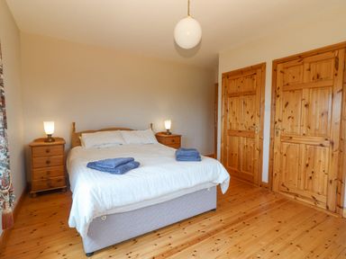 A bedroom with a bed and bedside tables with lamps and two wooden doors at Cloughoge House in Kilrush County Clare