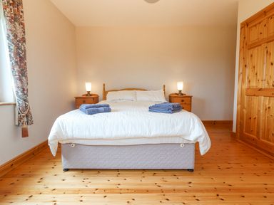 A bedroom with a double bed two bedside tables with lamps folded towels on the bed wooden floor and a wooden door at Cloughoge House in Kilrush County Clare