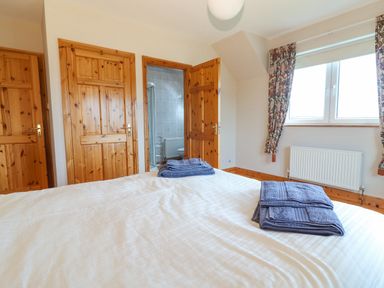 A bedroom with a bed folded towels on it wooden doors a window with patterned curtains and a bathroom at Cloughoge House in Kilrush County Clare