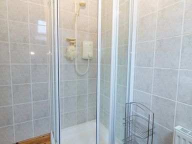 A shower enclosure with white tiles a shower head and metal shower caddy at Cloughoge House in Kilrush County Clare