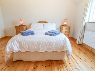 A bedroom with a bed with white bedding and blue towels on top two wooden bedside tables with lamps and a window at Cloughoge House Kilrush County Clare
