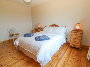A bedroom with a double bed white bedding blue towels wooden nightstands with lamps and a chair at Cloughoge House Kilrush County Clare