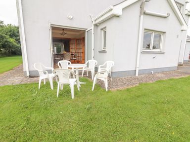 A patio area with white plastic chairs and a round table outside a house with an open door at Cloughoge House Kilrush County Clare