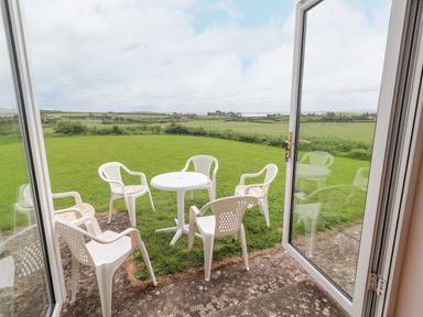 A patio with a round white plastic table and five white plastic chairs overlooking a grassy yard with fields in the background at Cloughoge House Kilrush County Clare