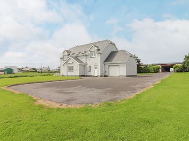 A detached two-story house with a garage and a large paved driveway surrounded by grass at Cloughoge House in Kilrush County Clare