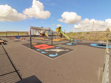 An outdoor playground with swings slides and play structures surrounded by a stone wall at Cloughoge House in Kilrush County Clare