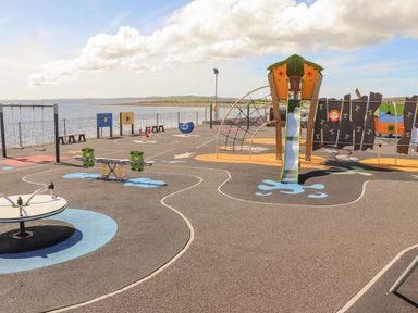 A playground with swings slide and climbing structures near water at Cloughoge House in Kilrush County Clare