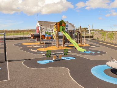 An outdoor playground with a slide climbing structures spring seesaw and a roundabout at Cloughoge House in Kilrush County Clare