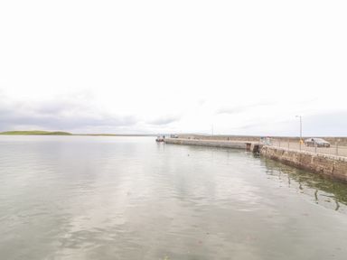 A stone pier extending into calm water with a small boat moored and a car on the pier at Cloughoge House in Kilrush County Clare