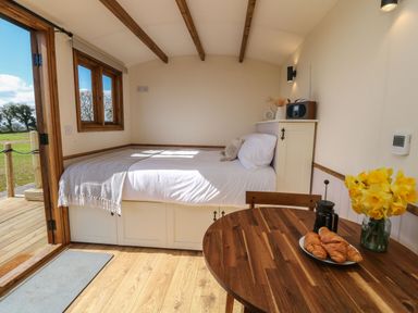 A small room with a bed near an open door a wooden table with croissants flowers and a coffee press at Buzzards in Morchard Bishop