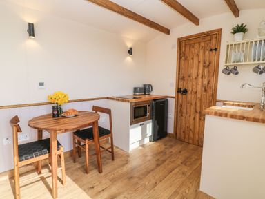 A kitchen with a wooden dining table and chairs a microwave toaster kettle and a wooden door at Buzzards in Morchard Bishop
