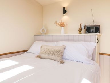 A bedroom with a bed a white pillow a cushion and a shelf with decorations at Buzzards in Morchard Bishop