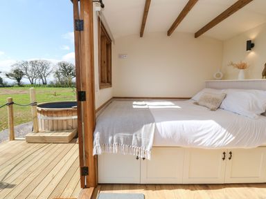 A bedroom with a bed next to open wooden doors leading to a deck with a wooden hot tub at Buzzards in Morchard Bishop