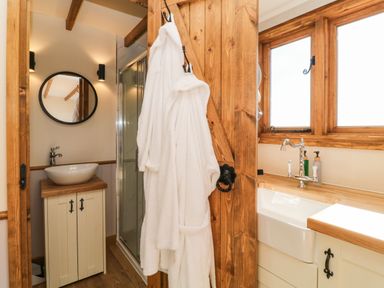 A bathroom with a sink, round mirror, shower enclosure, window, and two white robes hanging on a wooden door at Buzzards in Morchard Bishop
