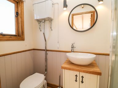 A bathroom with a high level toilet white basin on wooden countertop round mirror and wooden framed window at Buzzards in Morchard Bishop