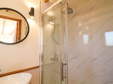 A bathroom with a round mirror a wall light a white sink and a glass shower enclosure with a rainfall showerhead at Buzzards in Morchard Bishop