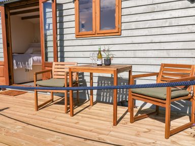 A wooden deck with two chairs and a table with a bottle and glasses outside a building at Buzzards in Morchard Bishop