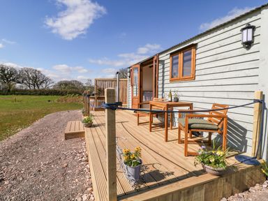 A wooden deck with chairs and a table outside a small wooden building at Buzzards in Morchard Bishop