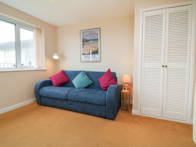 A room with a blue sofa with cushions a lamp a floor lamp a window a framed picture and a white closet at Sky Pocket in Bude