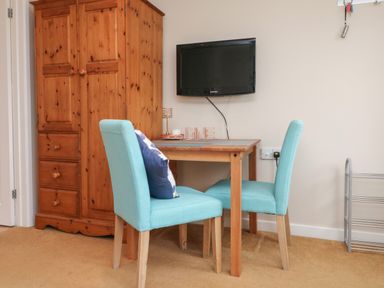 A small dining area with a wooden table and two turquoise chairs near a wooden wardrobe and a wall-mounted TV at Sky Pocket in Bude