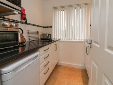 A kitchen with black countertop white cabinets a toaster an oven kettle and a window with vertical blinds at Sky Pocket in Bude