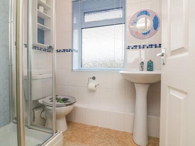 A bathroom with a shower cabin toilet sink window with blinds and a round mirror at Sky Pocket in Bude