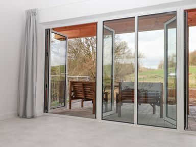 A room with large glass folding doors opening to an outdoor patio with wooden benches at Narracott Down in South Molton