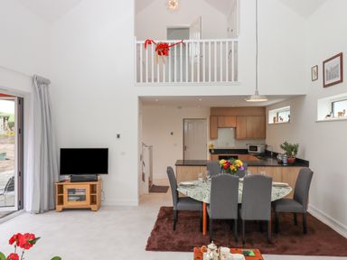 A dining area with a table and six chairs near a kitchen with wooden cabinets and a TV on a stand at Narracott Down in South Molton