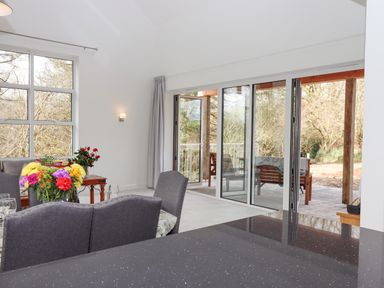 A dining area with grey chairs a table with flowers and large windows opening to a patio at Narracott Down in South Molton
