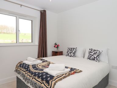 A bedroom with a bed with folded towels cushions and a blanket near a window with brown curtains at Narracott Down in South Molton