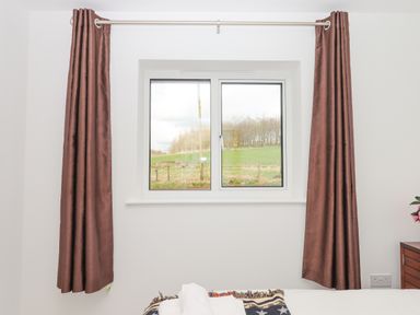 A bedroom window with brown curtains and a bedside table with flowers at Narracott Down South Molton
