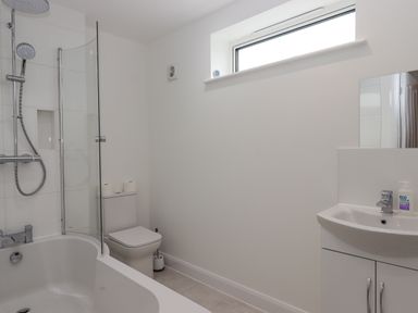 A bathroom with a bathtub and shower, a toilet, a sink with a cabinet, and a window at Narracott Down in South Molton
