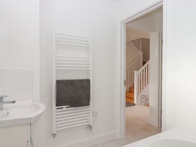 A bathroom with a white sink and towel radiator with a dark towel and a view of stairs at Narracott Down in South Molton