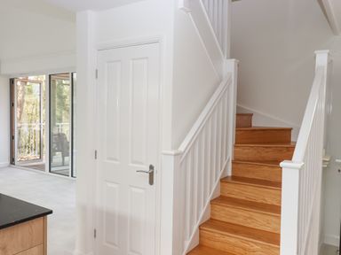 A wooden staircase with white railing next to a closed white door and glass doors leading outside at Narracott Down in South Molton