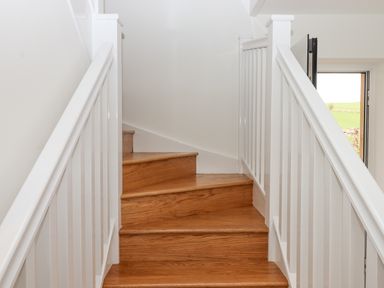 Wooden staircase with white railings and a partially visible open door showing outside at Narracott Down in South Molton