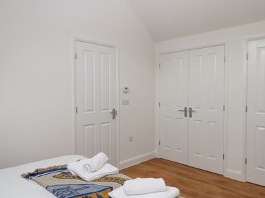 A bedroom corner with three white paneled doors a bed with folded towels and a blanket on a wooden floor at Narracott Down in South Molton