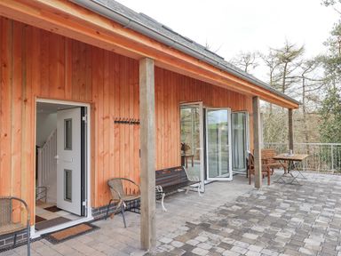 An outdoor patio area with wooden chairs a bench a table and glass doors opening to the interior at Narracott Down in South Molton