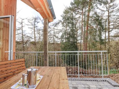 An outdoor wooden table and bench set with a metal coffee pot and cups on a tray on a patio with a metal railing and trees in the background at Narracott Down in South Molton