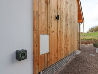 An exterior wall with grey and wooden panels and an electric car charging station at Narracott Down in South Molton