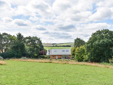 A house with a sloped roof surrounded by trees and green fields at Narracott Down in South Molton