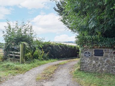 A gravel driveway bordered by hedges and a stone wall with a narracott down sign in south molton