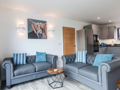A living room with two grey sofas with blue cushions and a round wooden coffee table at Strawberry Bank - Nuthatch in Pyworthy near Bridgerule