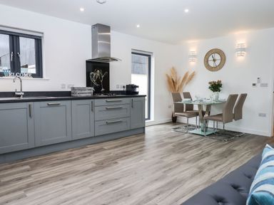 A kitchen and dining area with grey cabinets a glass dining table and beige chairs at Strawberry Bank - Nuthatch in Pyworthy near Bridgerule