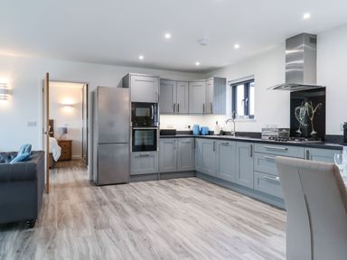 A kitchen with grey cabinets and countertops a stainless steel refrigerator a built-in oven and microwave a stove with a stainless steel hood and a window above the sink at Strawberry Bank - Nuthatch Pyworthy near Bridgerule